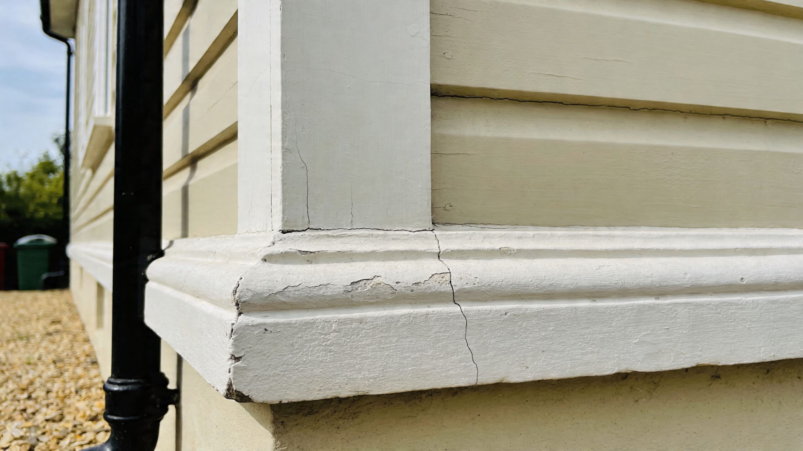 En revnet malet hjørneafslutning på en bygnings sokkel med synlige skader i malingen og træværket.