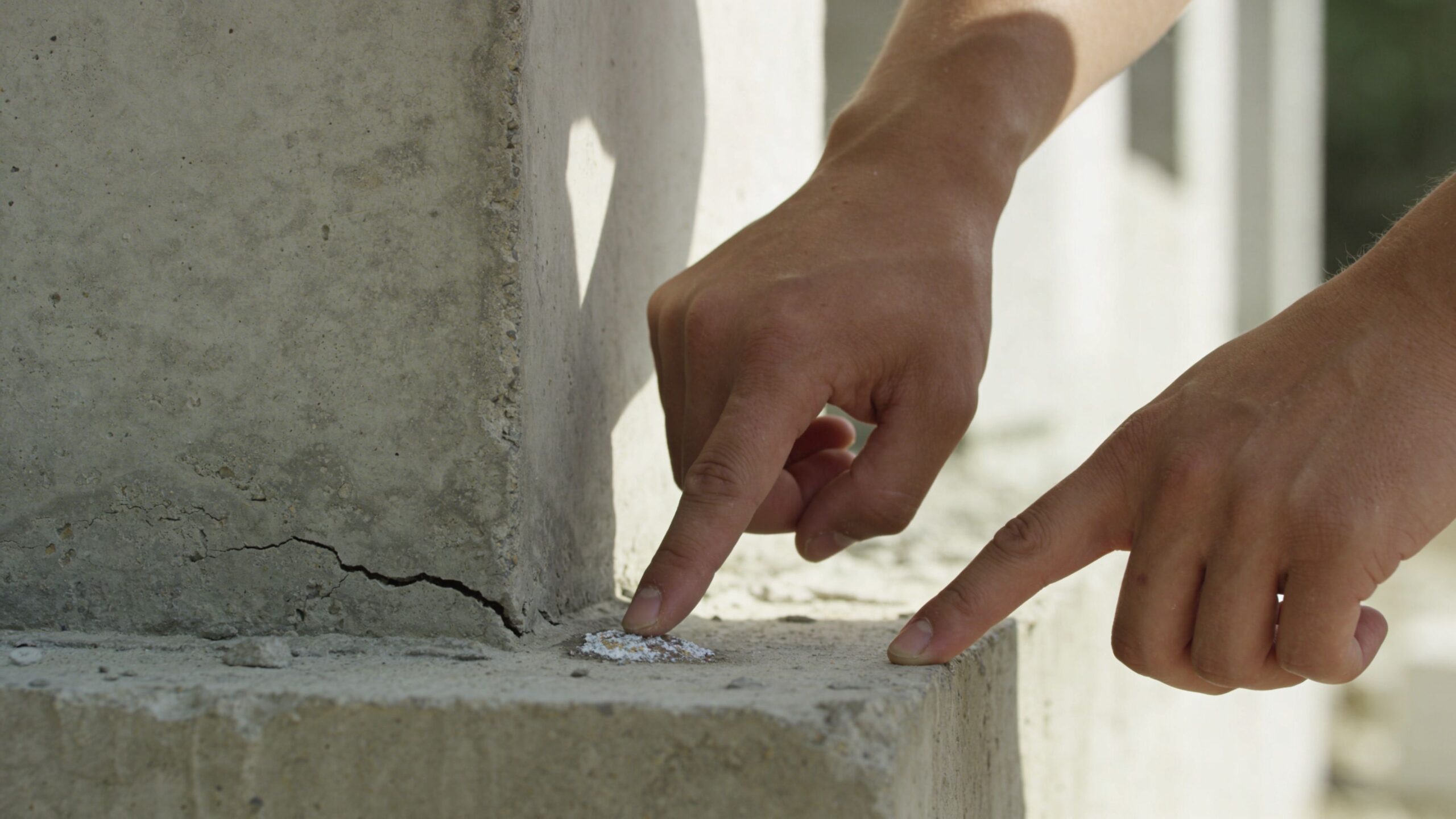 En person peger på en synlig revne ved fundamentet af en betonkonstruktion på en byggeplads.
