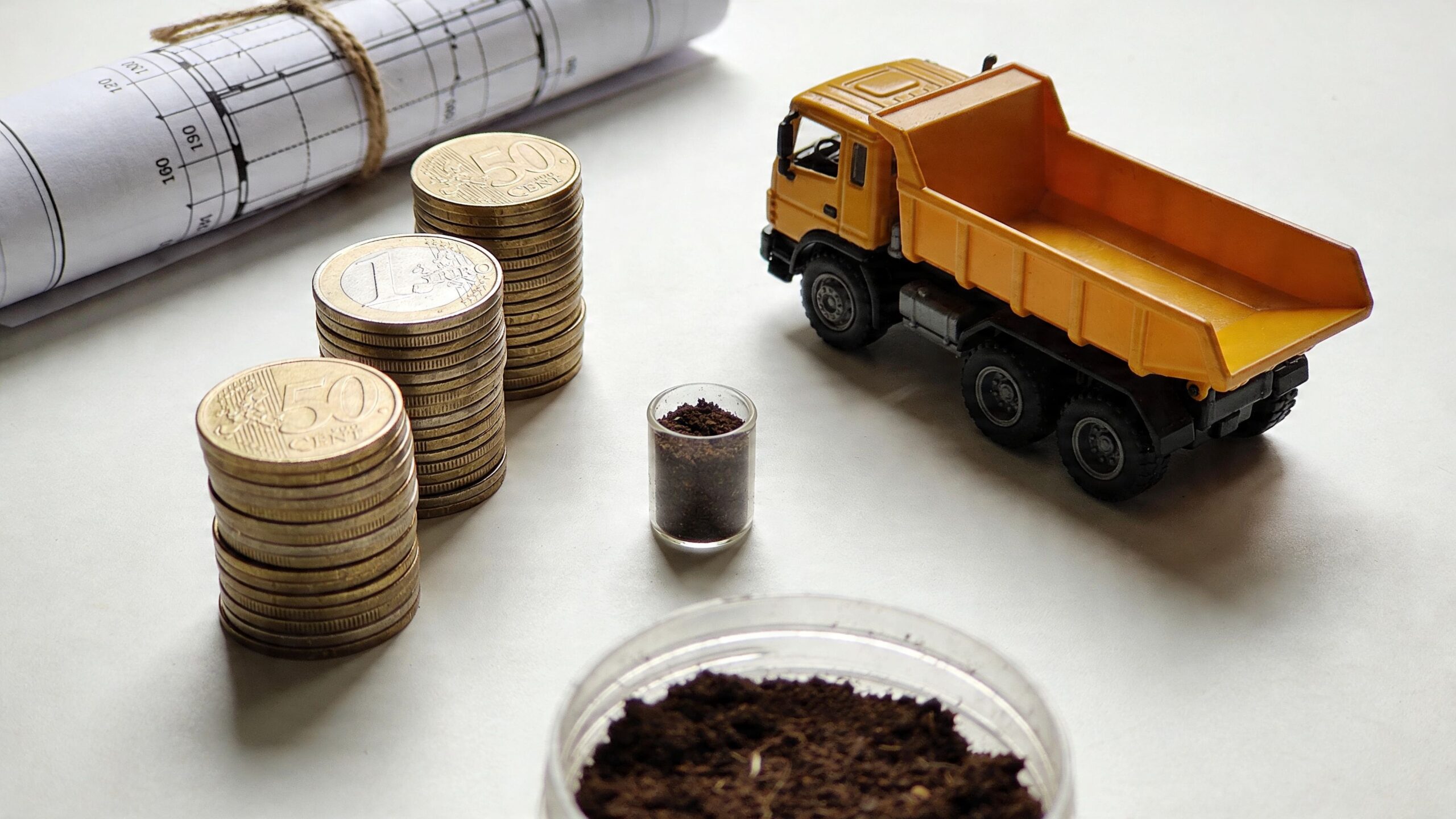 En legetøjslastbil ved siden af mønter og en tegning, der symboliserer omkostninger ved bortkørsel af jord.