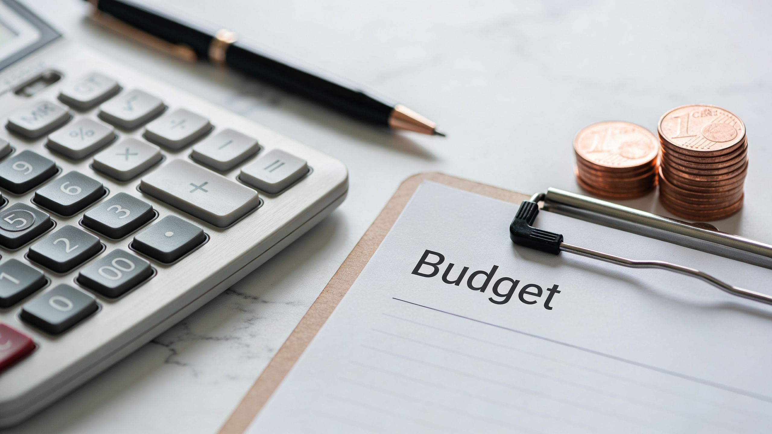 En lommeregner, en pen og en stak mønter ved siden af en blok med ordet Budget skrevet.